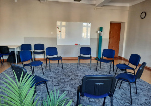 Sala 105, duża sala z krzesłami do zajęć grupowych. Niebieskie krzesła ustawione w kręgu, tablica.